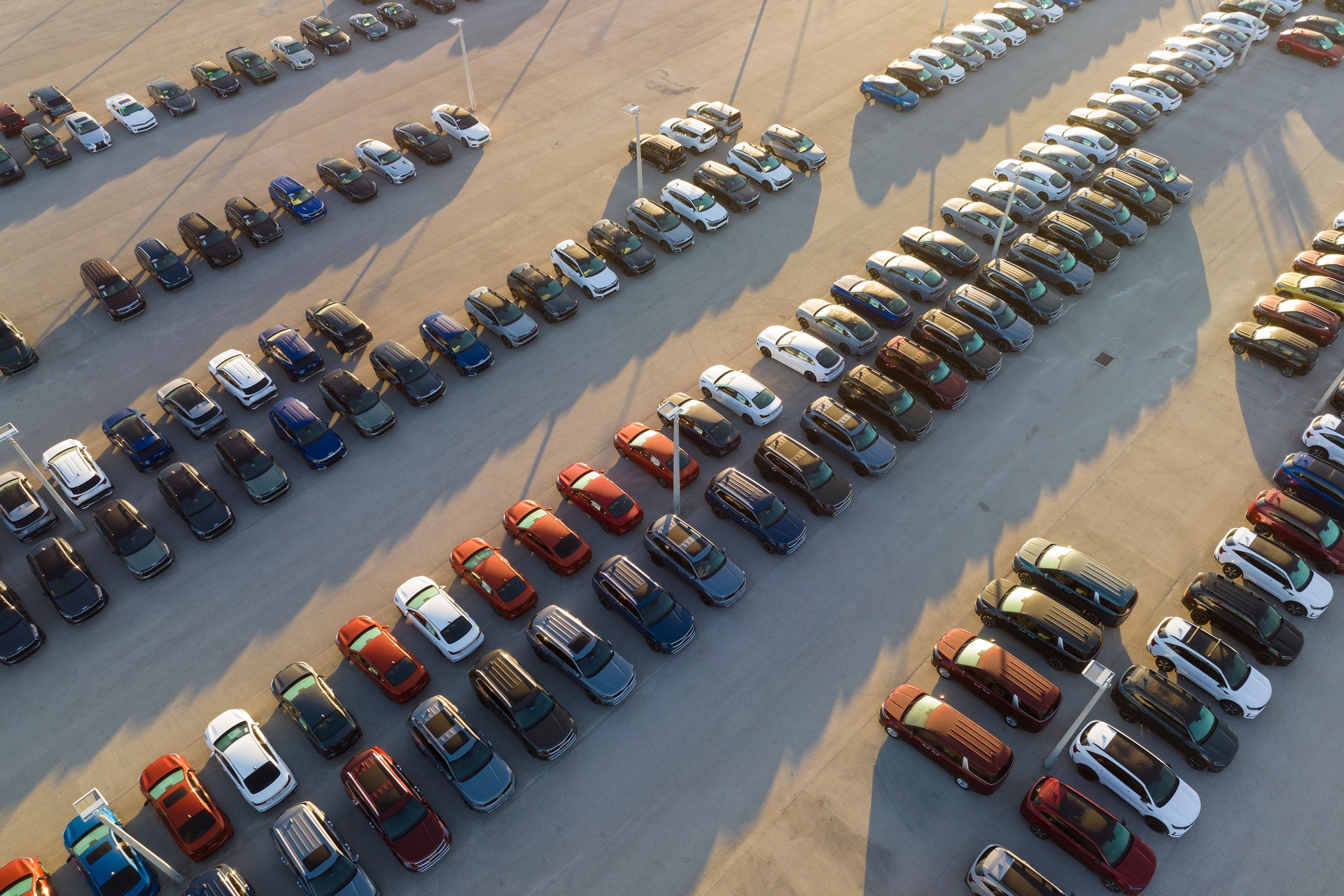 Large parking lot of local dealer with many brand new cars parked for sale. Development of american automotive industry and distribution of manufactured vehicles concept